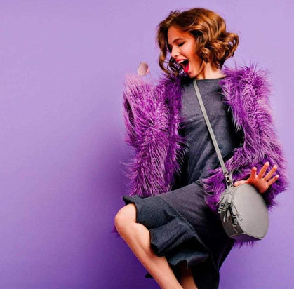 Woman in a purple fur coat holding a handbag against a purple background